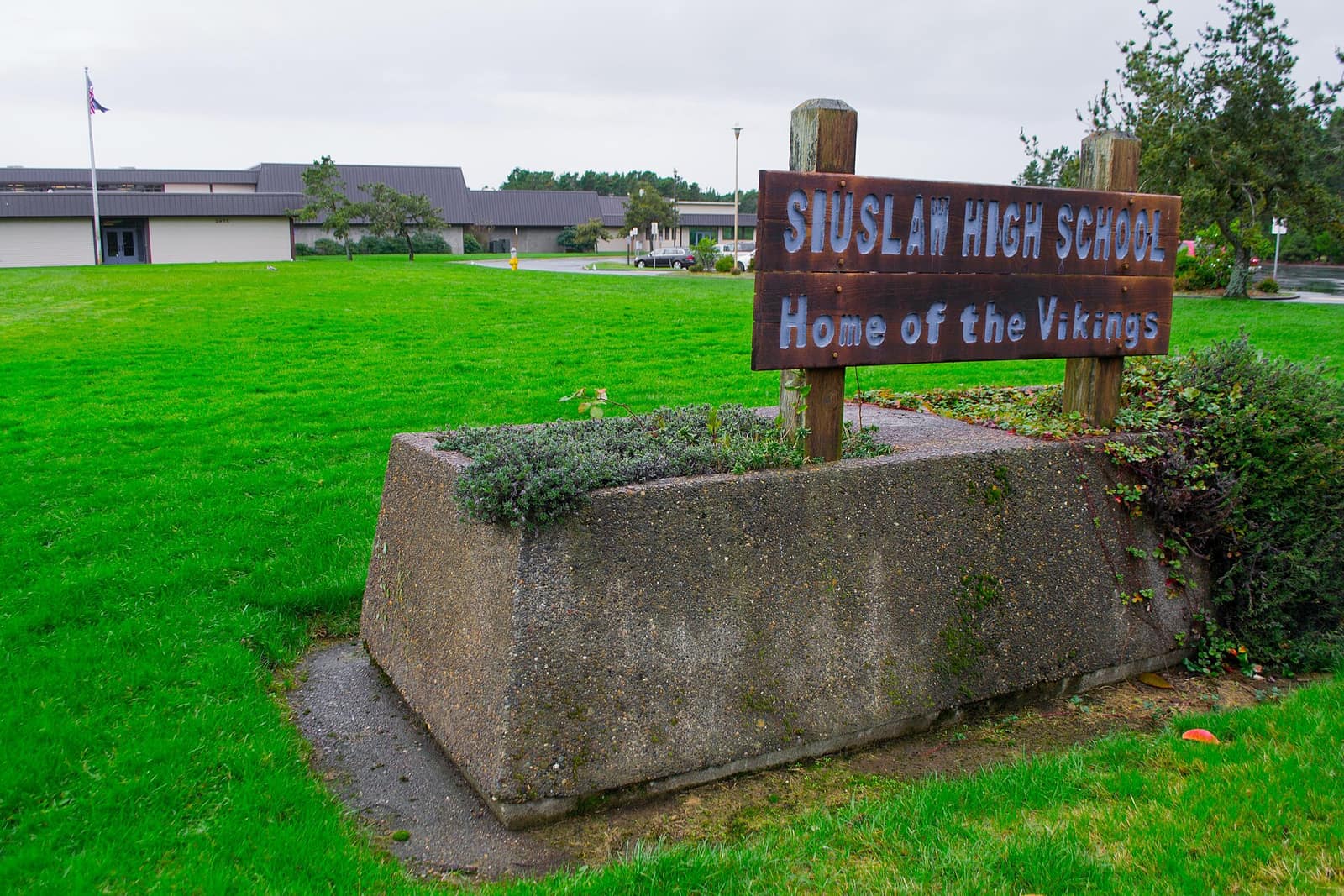 The Siuslaw High School sign, Home of the Vikings, on a lawn with school buildings behind