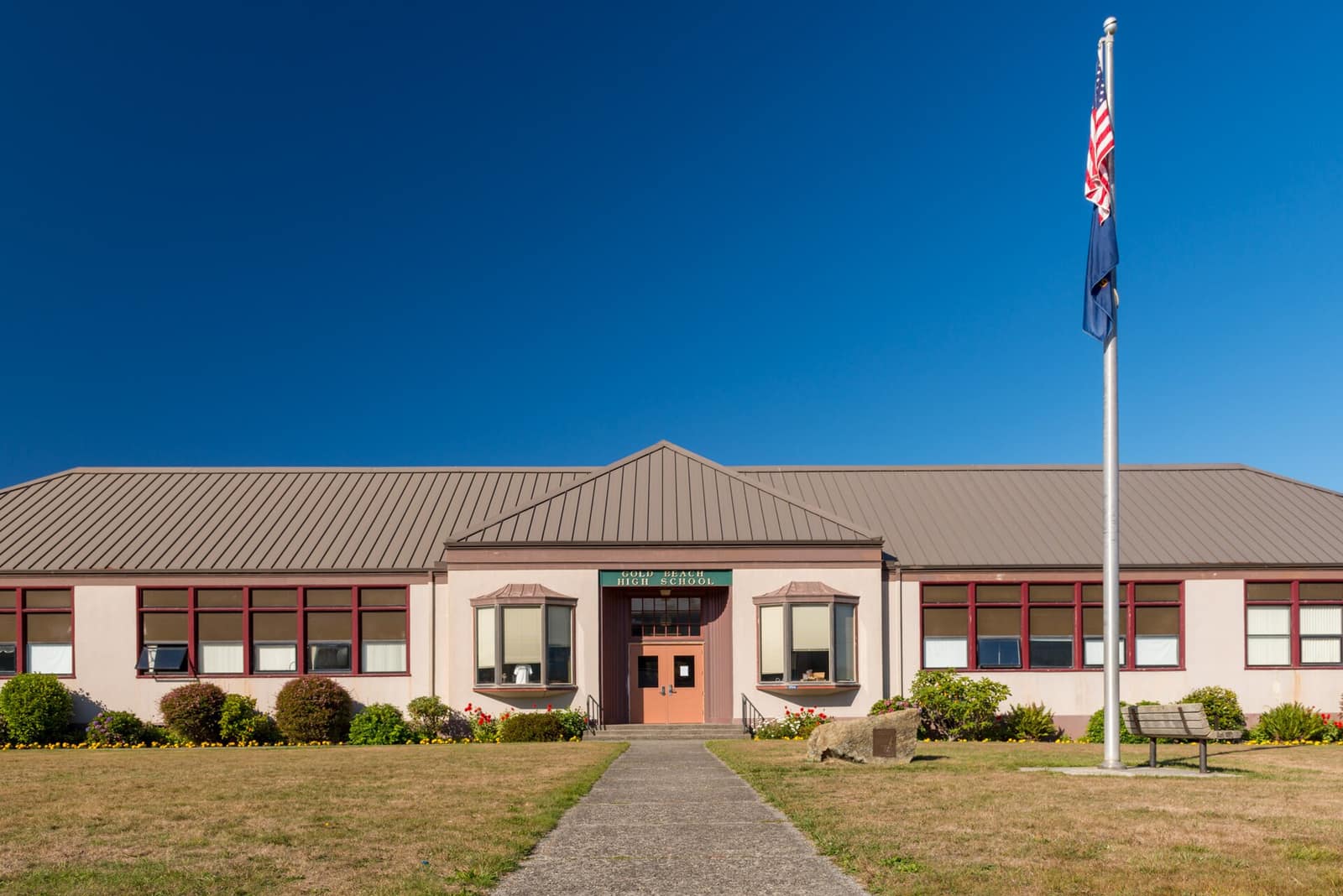 The front entrance of Gold Beach High School, a low building with a metal roof, a flagpole and a lawn