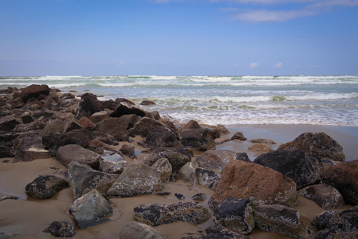 Surf rolling onto a beach strewn with dark rocks near Newport