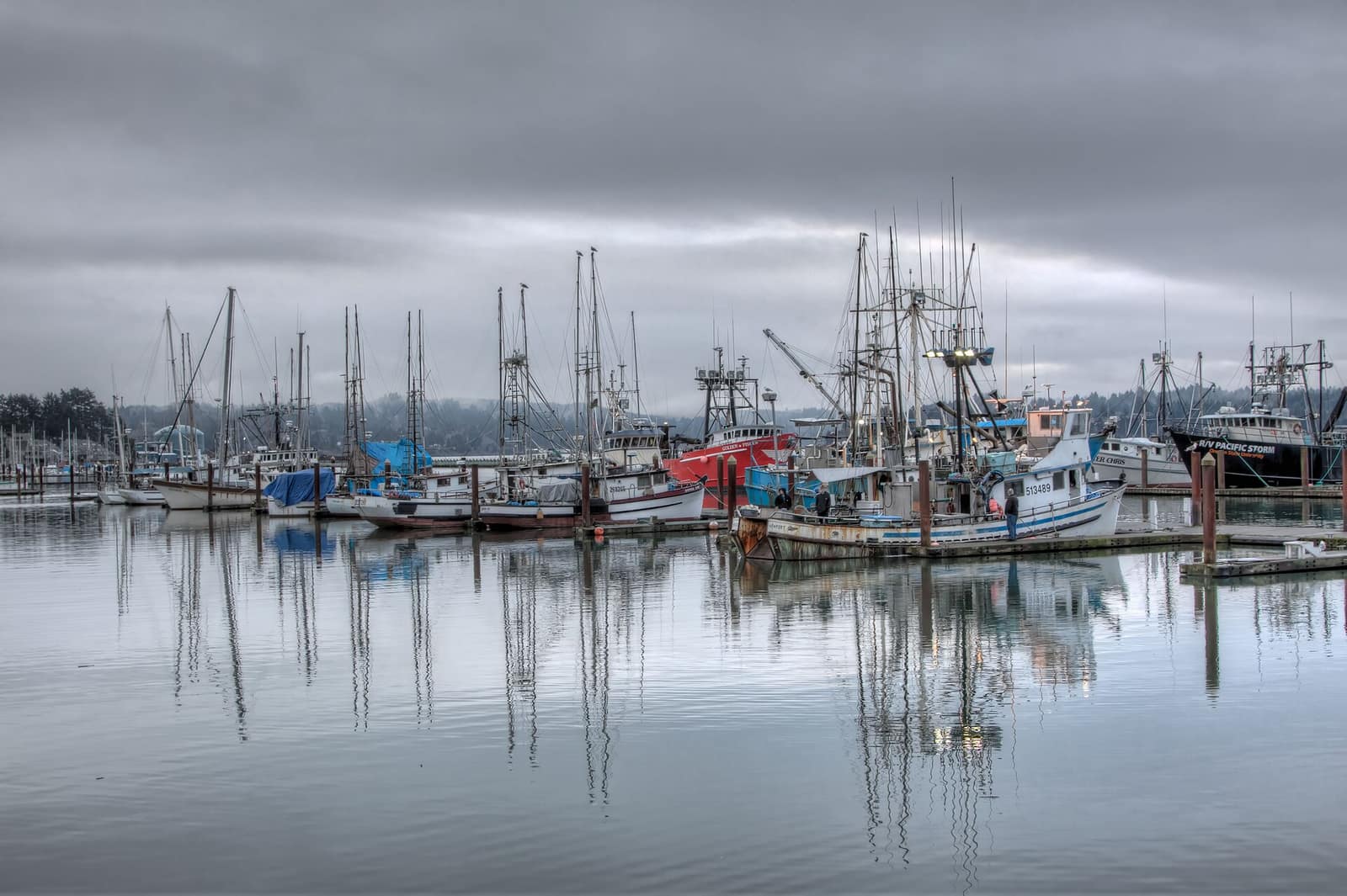 Fishing boats and masts reflected in calm water under heavy cloud at the Newport harbor