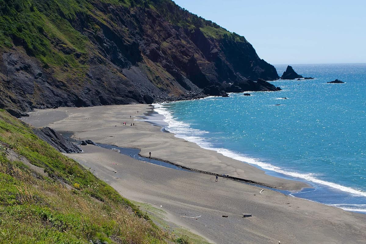 A broad sandy beach and a rocky cliff with the ocean at right on the south Oregon coast