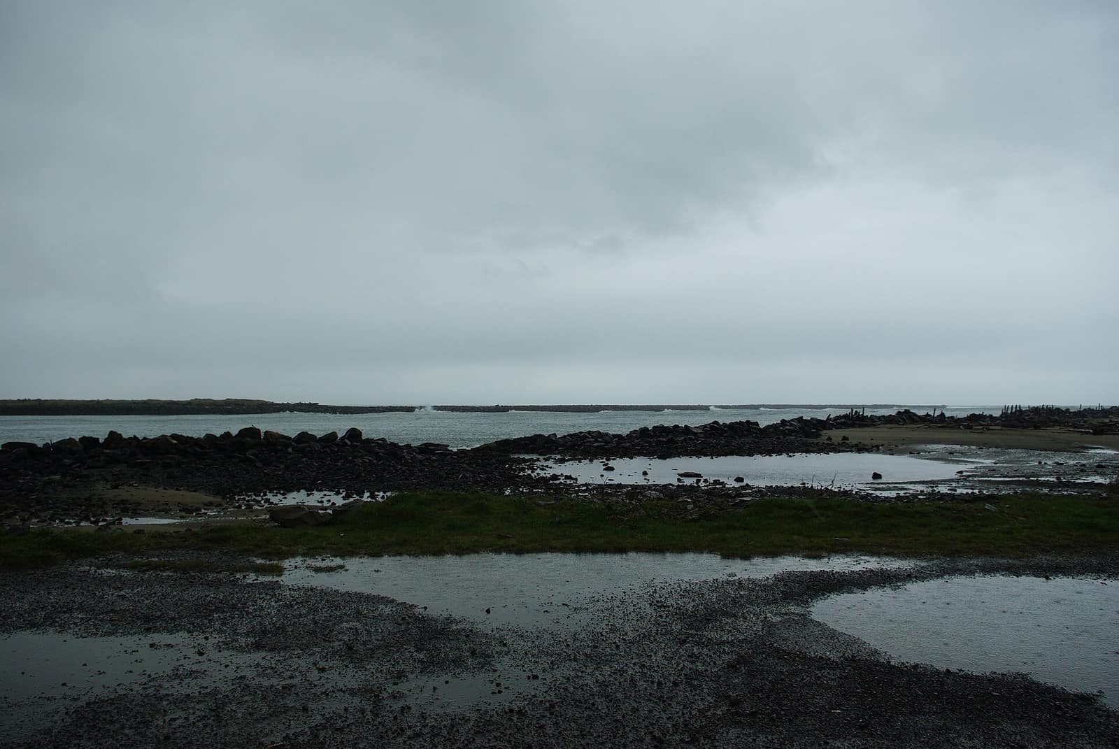 Rocks and tidal pools in rain with the jetties at the entrance to Tillamook Bay in the distance